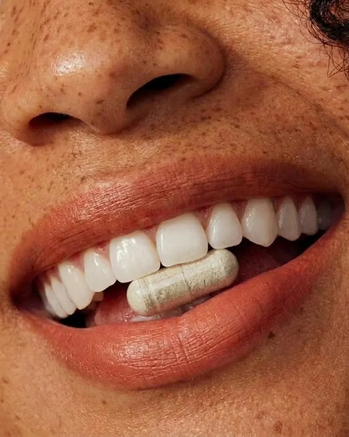 A close-up of someone holding a capsule between their teeth