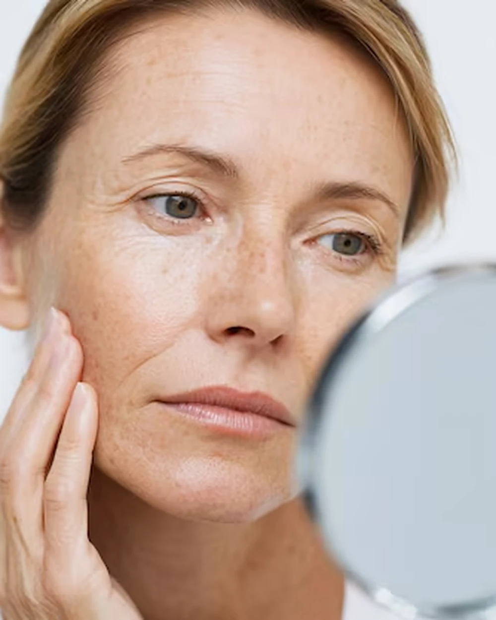 A woman looking at her skin in a hand mirror